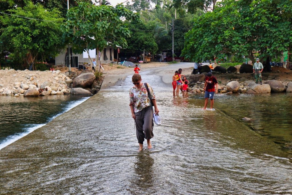 a woman walks through a road cut by a stream in the south of thailand