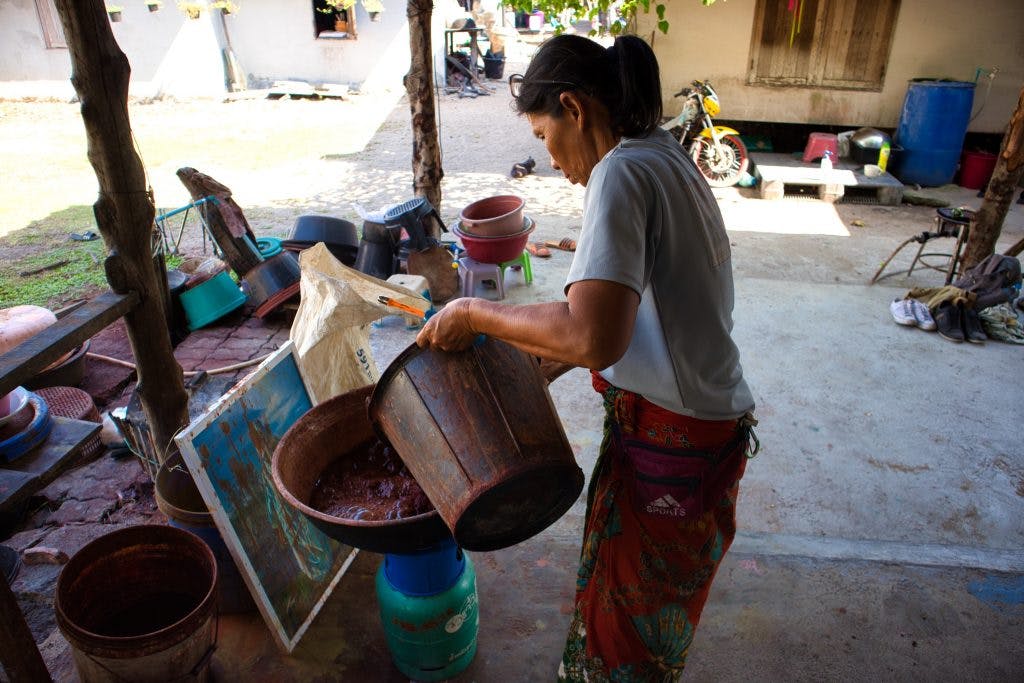 a thai woman is making dye using natural ingredients. she is holding a plastic bucket and pouring water in a bowl. thailand, krabi, koh klang. 