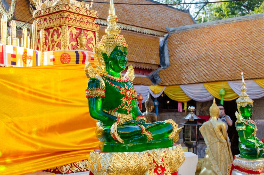 Zielony posąg Buddy siedzi przy stupie w świątyni Doi Suthep, Chiang Mai.