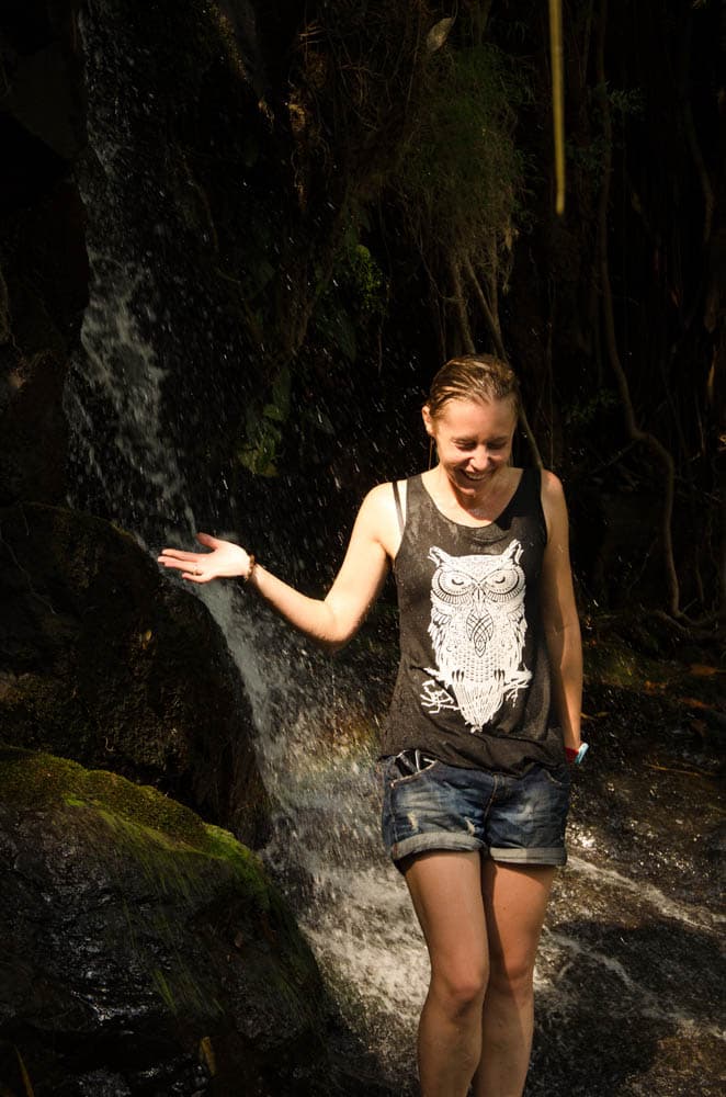 a woman standing under a waterfall in a top and shorts lauhing, in mea hong song, thailand 