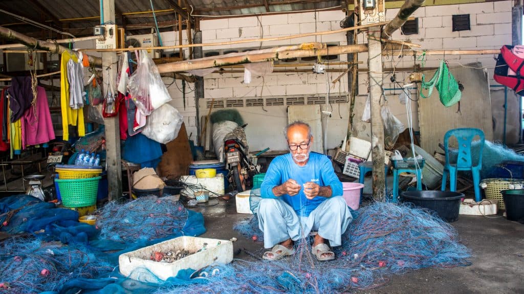 Old Thai fisherman fixing nets.