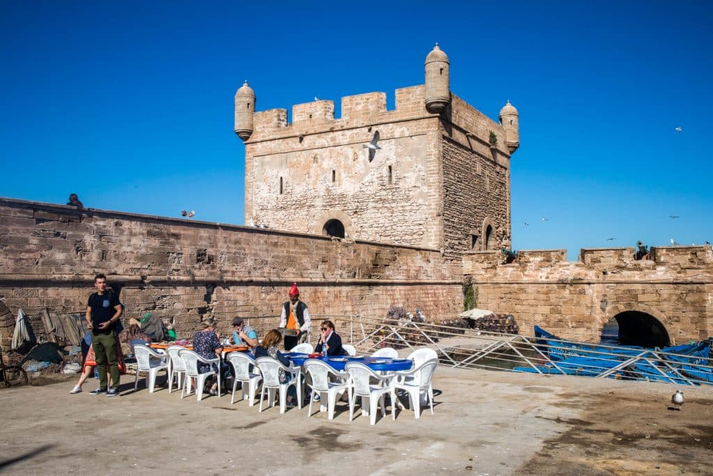 portowa restauracja w eussaouira. ludzie siedzą na zewnątrz przy murach miasta. 