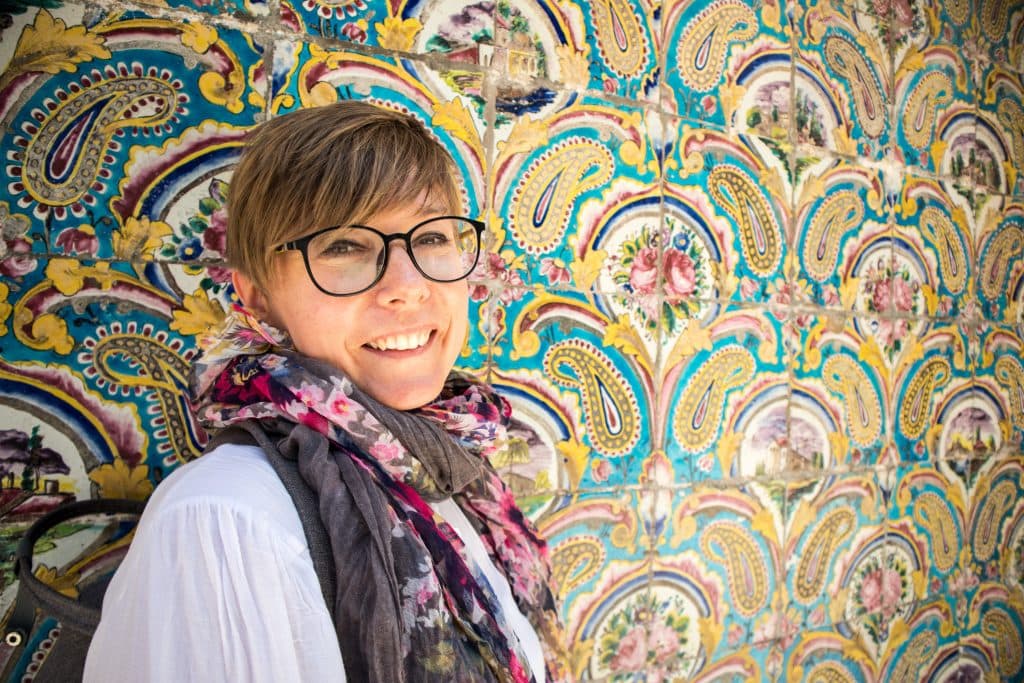 a girl standing in front of a beautifully ornamented yellow wall in iran 