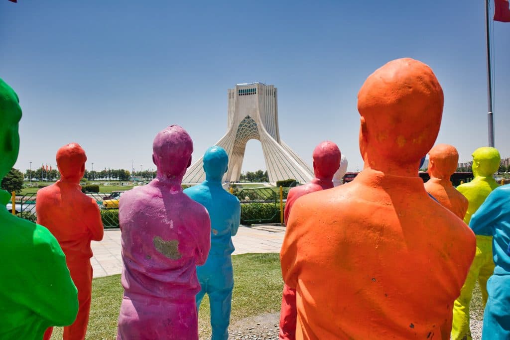 azadi tower seen from the other side of the street, behind colourful statutes