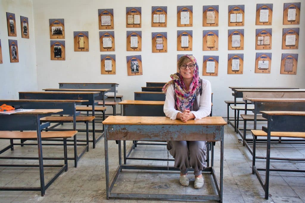 a smiling girl sits behind an old desk in the house of techniques in teheran iran.