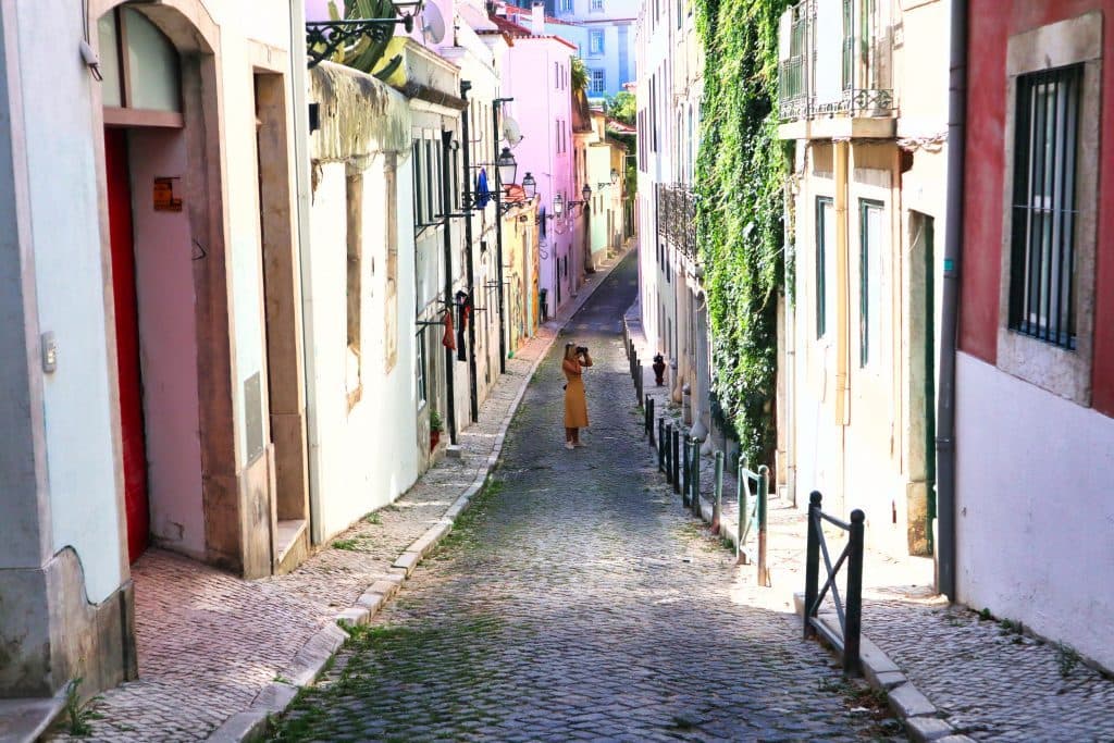 a girl in a yellow dress photographs a pink house in lisbon, portugal