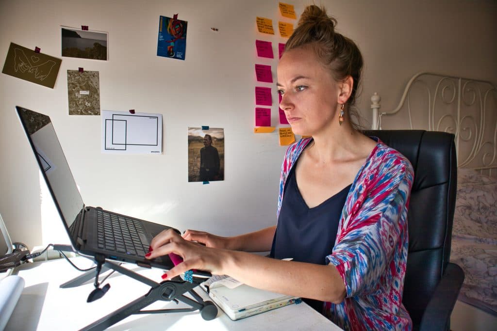 a girl in a colourful jumper sits in her room and works on her laptop