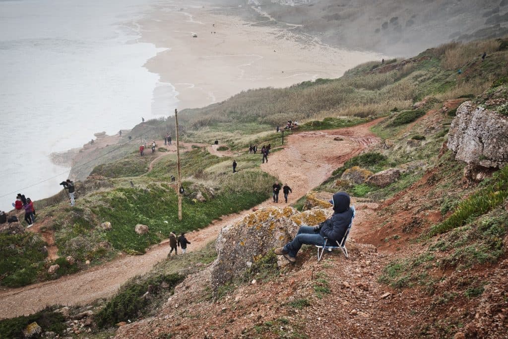 a man sitting on a chair watching waves in nazare, portugal