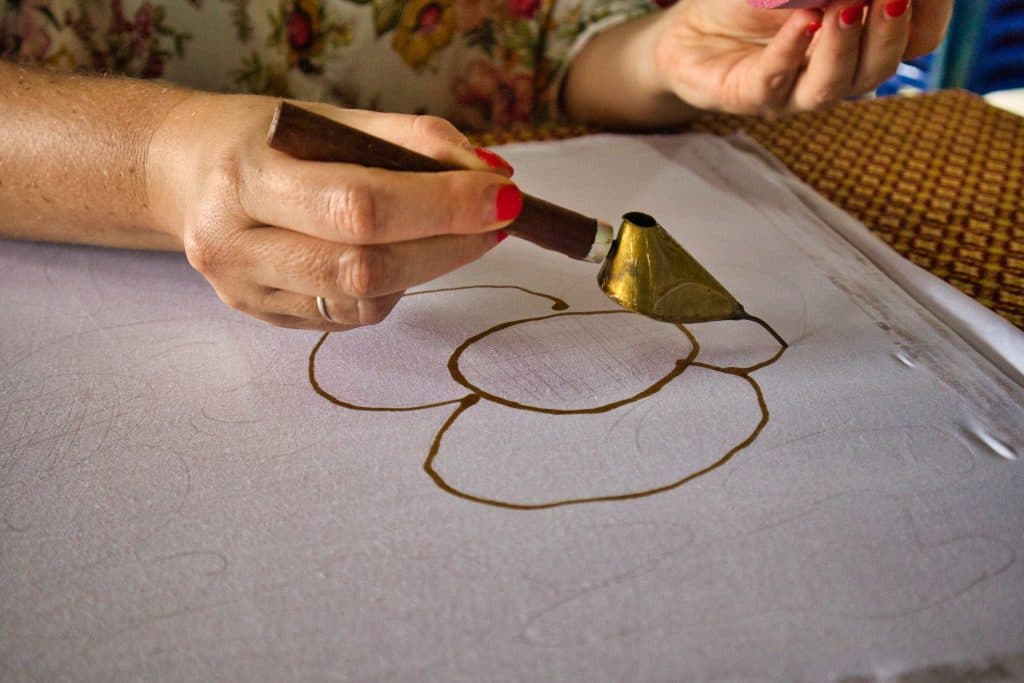 a hand holding a metal tool to draw with a wax on canvas