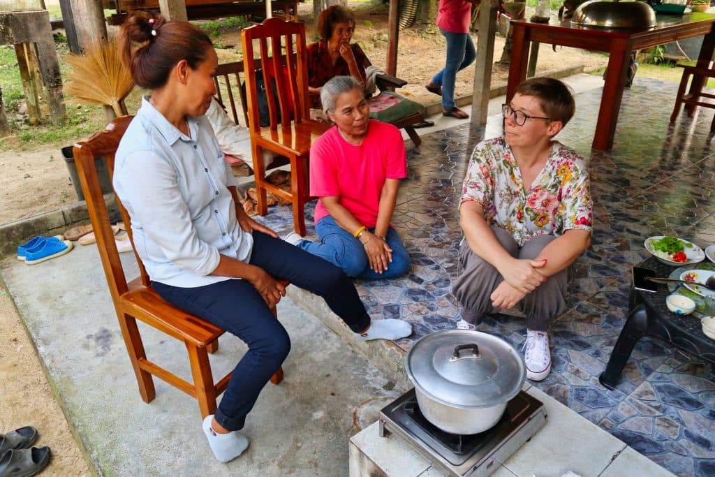 Two thai women talking to a tourist while cooking in a Thai village in nakhon si thammarat province. 