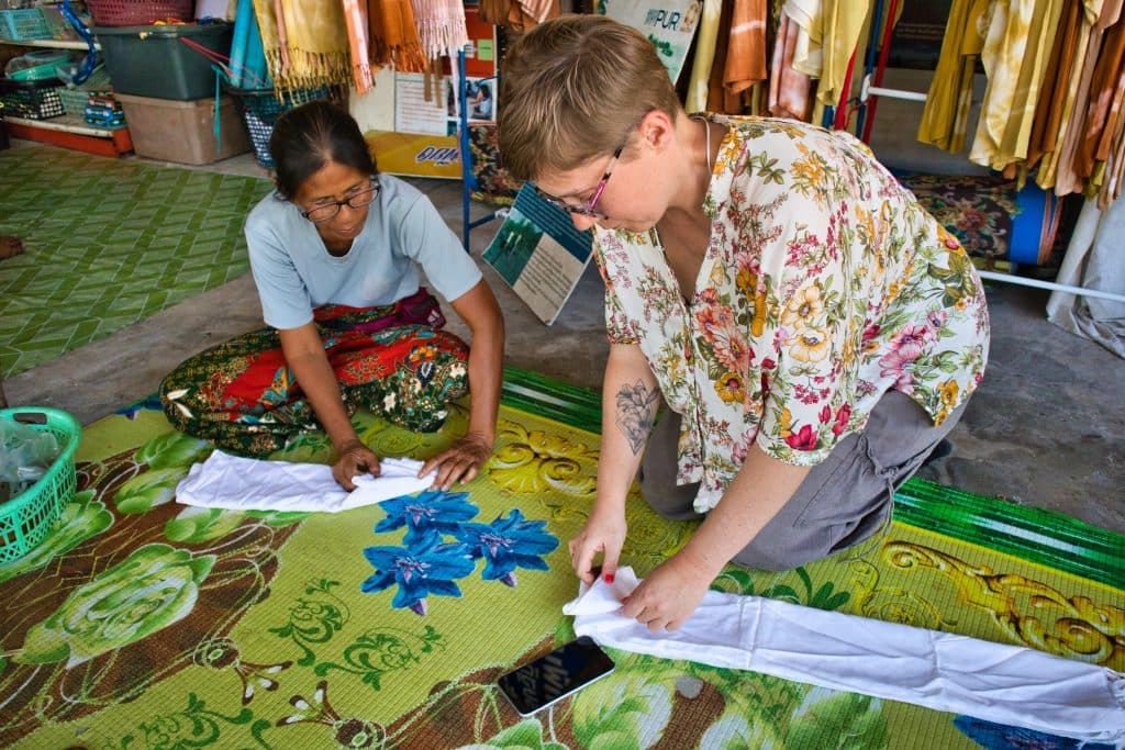 a thai woman and foreign woman are sitting on a floor and folding a white material.  