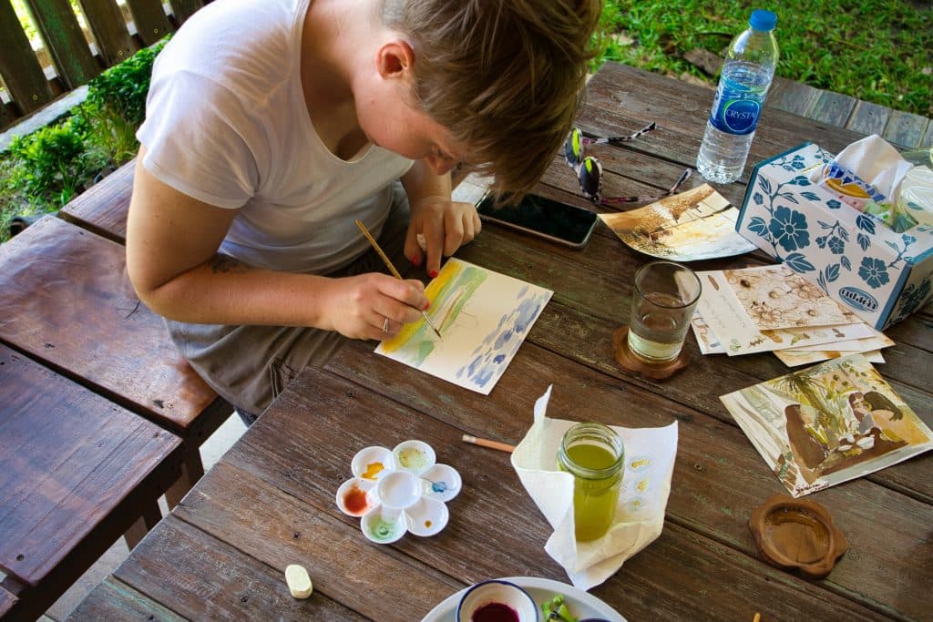 a woman painting a postcard with natural colours in koh klang, thailand. 