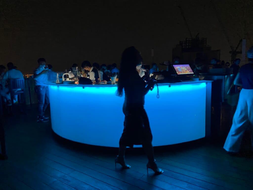 Rooftop w bangkoku. Kobieta na wysokich obcasach przechodzi obok baru. 