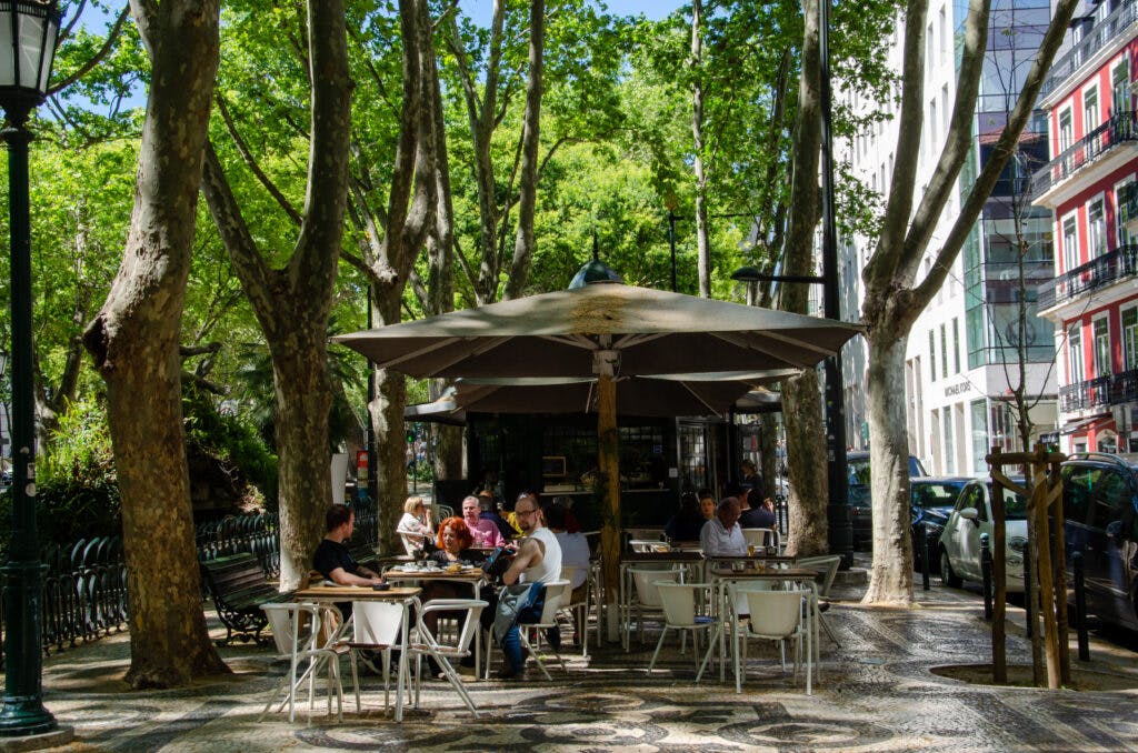 People sitting at tables near a kiosk in Lisbon. 