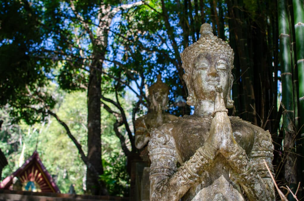 Posąg Buddy w ruinie świątyni niedaleko Chiang Mai. Za posągiem widać fragment świątyni oraz las. 