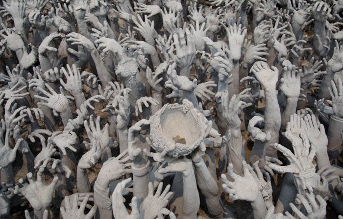 sculptures of hands coming out of the ground at the white temple in chiang rai