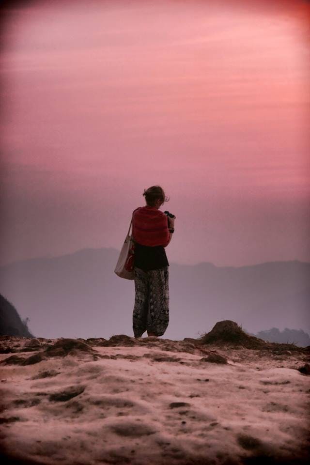 a woman with a camera standing on an edge of a mountain in thailand 