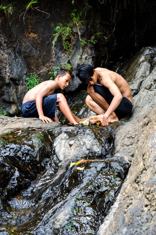 two boys playing at a waterfall in mea hong song, thailand 