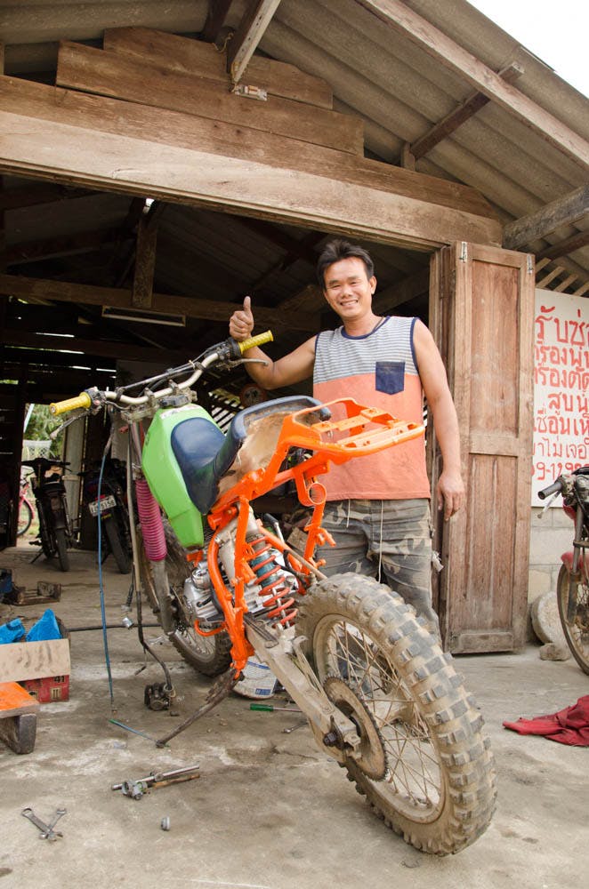 a man standing at his bike in a motorbike workshop in chiang dao, thailand 
