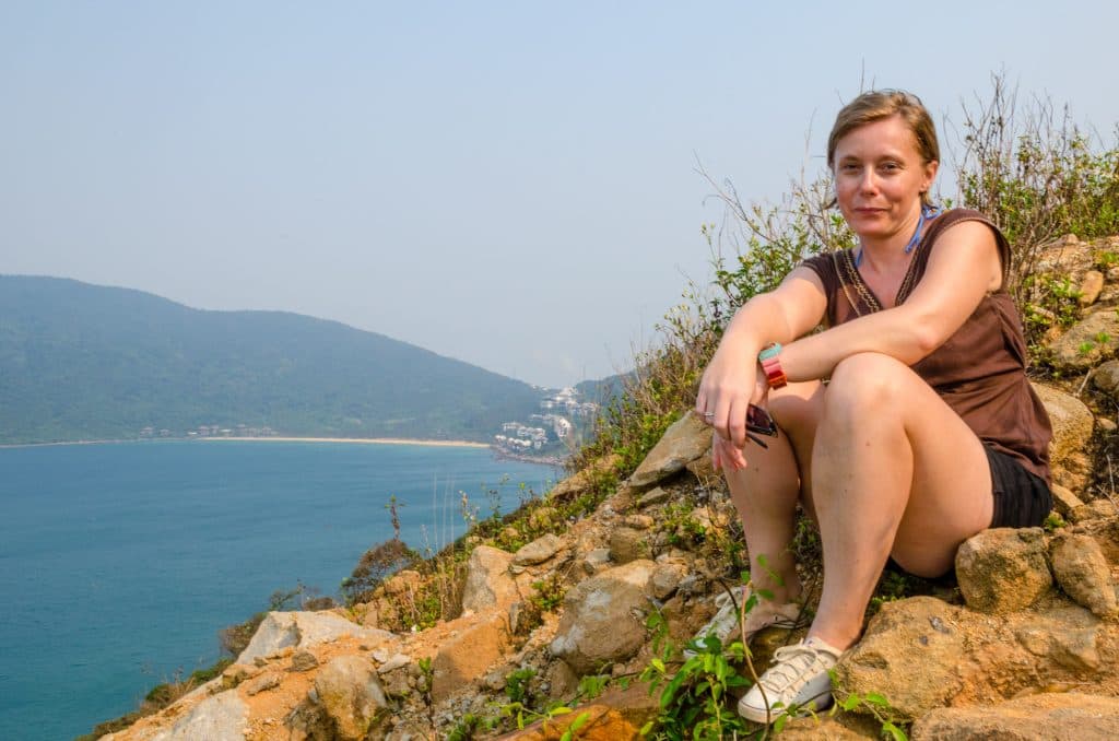 A woman in a brown top and shorts sits on a rock overlooking the water in Vietnam.