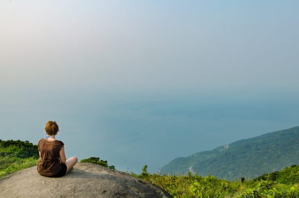 A woman in a brown top sits on top of a rock overlooking the sea in son tra peninsula.
