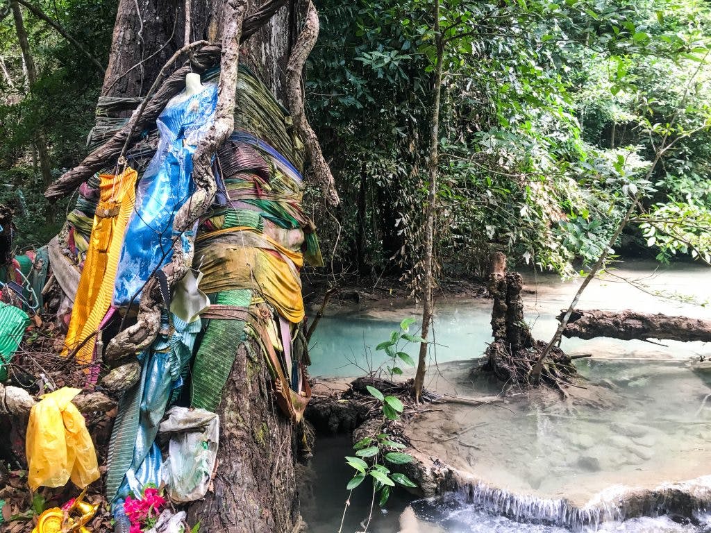 erawan waterfall colourful clothes attached to a tree with emerald water flowing