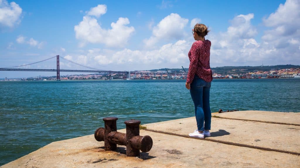 a girl standing in almada looking at the bridge in lisbon