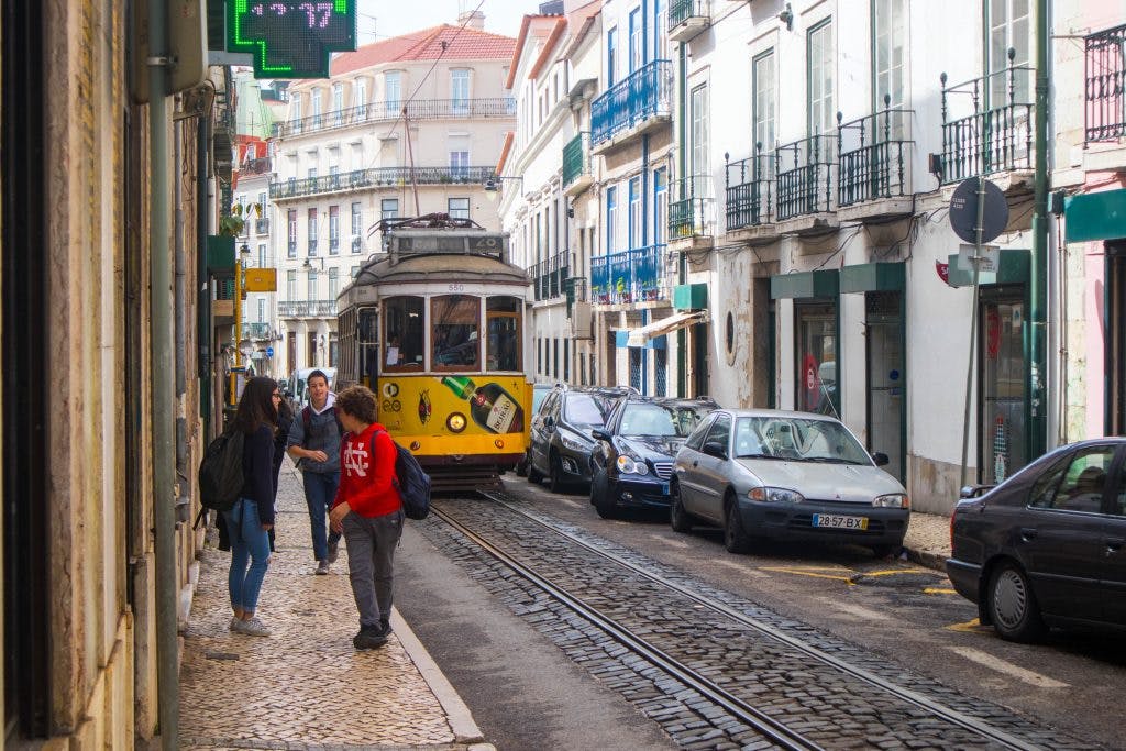 yellow tram drives through the street of lisbon passing people