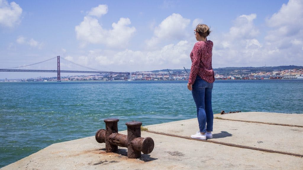 joanna stoi na wybrzezu i patrzy na most 25go kwietnia w lizbonie