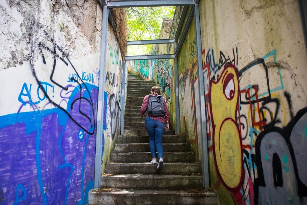 a girl in a purple shirt and jeans walks up the stairs in almada lisbon