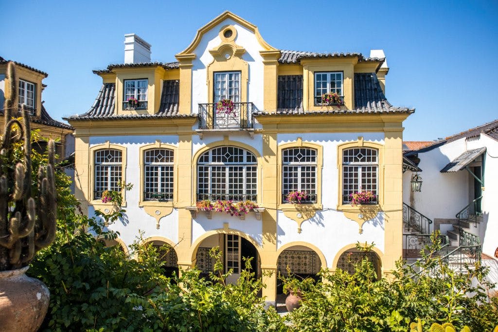 Zółto-biały dom José Maria de Fonseca w Azeitao otoczony roślinnością w słoneczny dzień. 