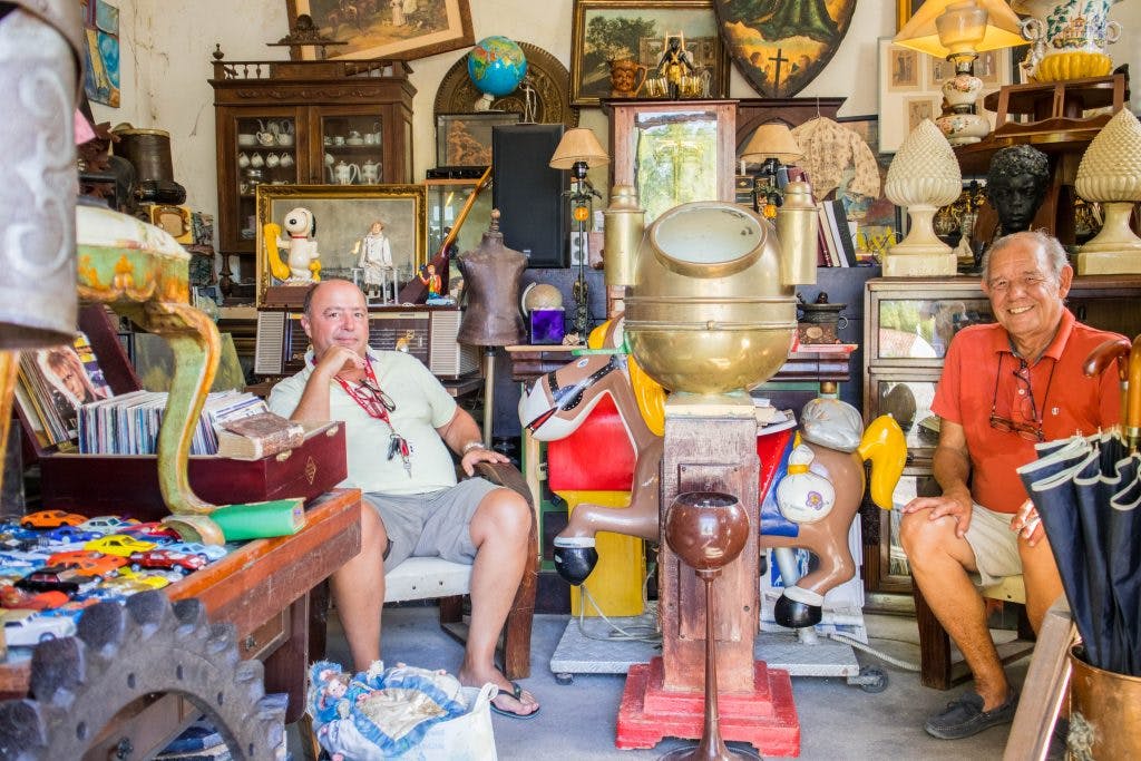 Dwoch opalonych mezczyzn w letnich ubraniach siedzi w sklepie ze starociami w Azeitao. 