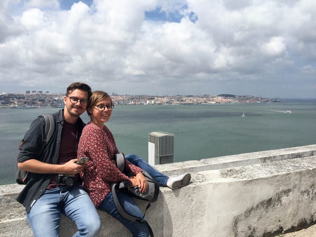 a couple sits on a wall on a viewpoint in almada lisbon