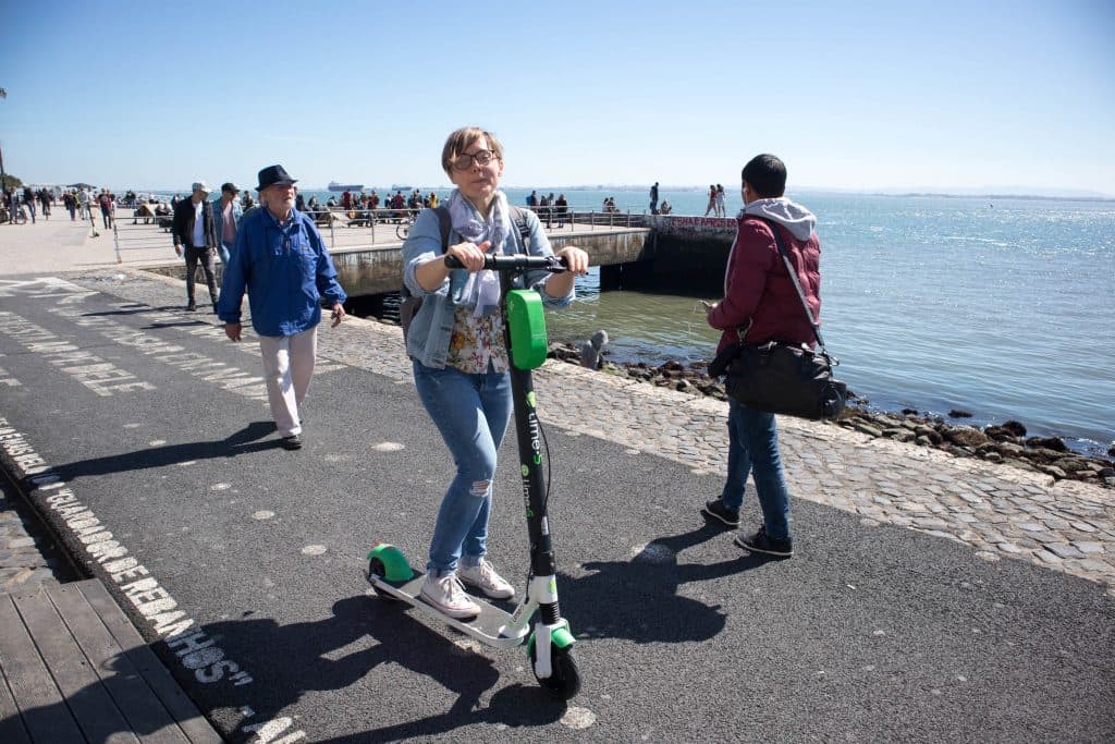 a girl on a lime scooter on a sunny day at the river in lisbon