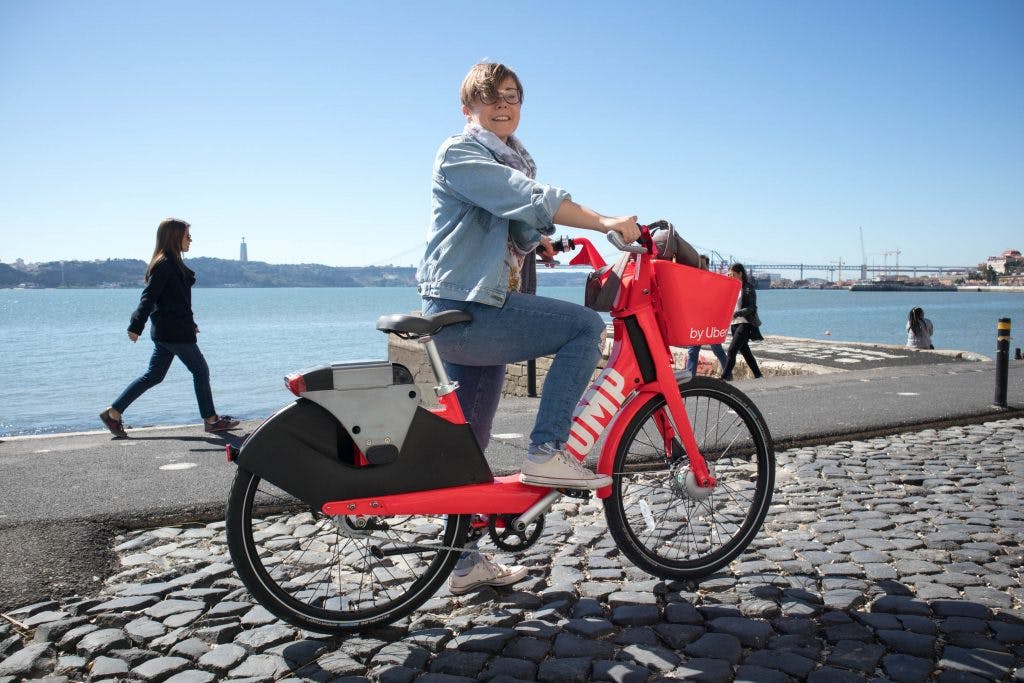 a smiling girl on a red uber bike at the river in lisbon 