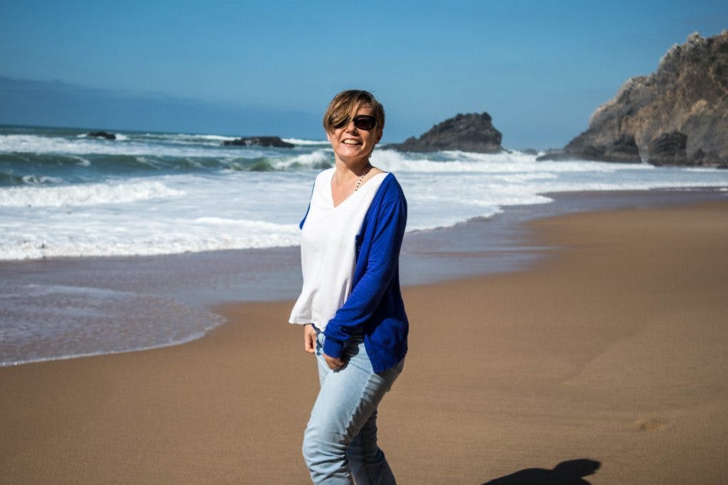 a girl in a blue jumper laughs on adraga beach in portugal 