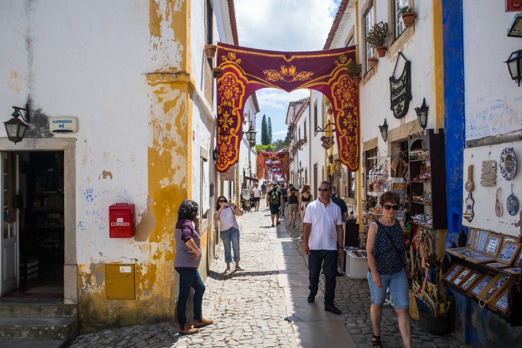 a street in obidos with hanging banners and people walking 