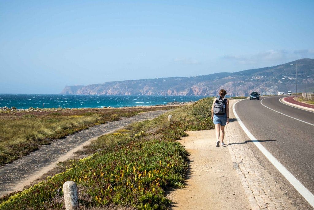 a girl walks from cascais to guincho by the side of the road with the ocean on her left. 