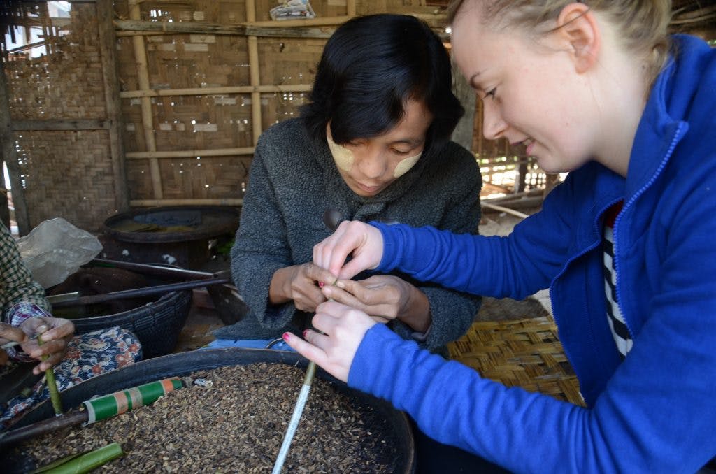 a girl in a blue jumper is making a cigar with a burmese lady 