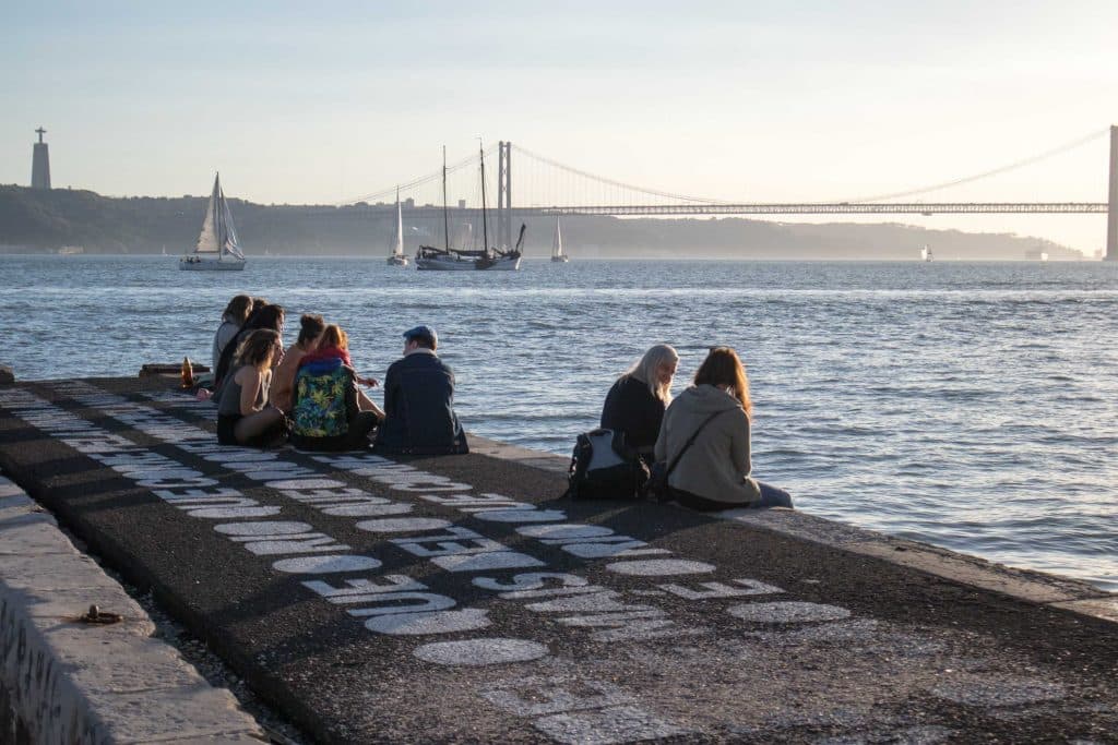 people sitting on the shore of the tagus river in Lisbon in the evening.
