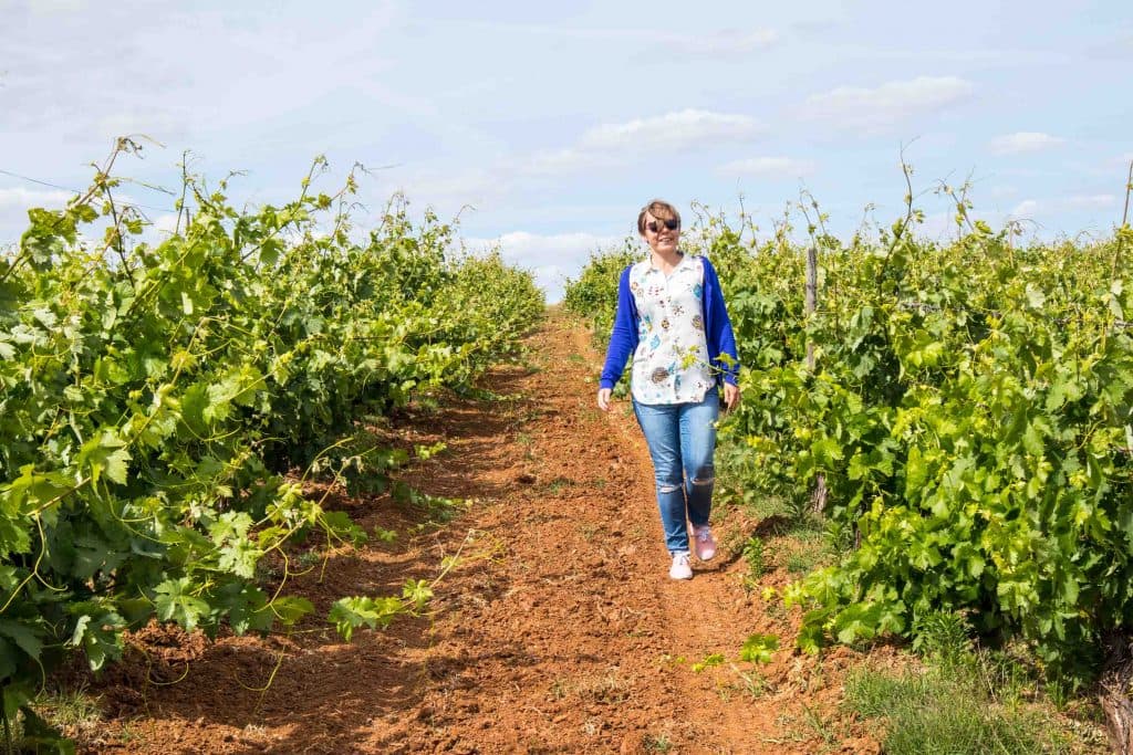 usmiechnieta dziewczyna w niebieskim sweterku idzie wzdluz winorosli w alentejo