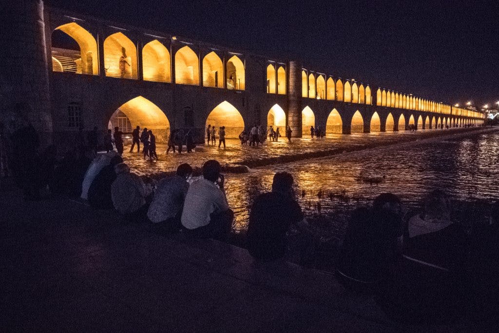 Ludzie siedzą nad rzeką przy oświetlonym moście w Esfahan. 