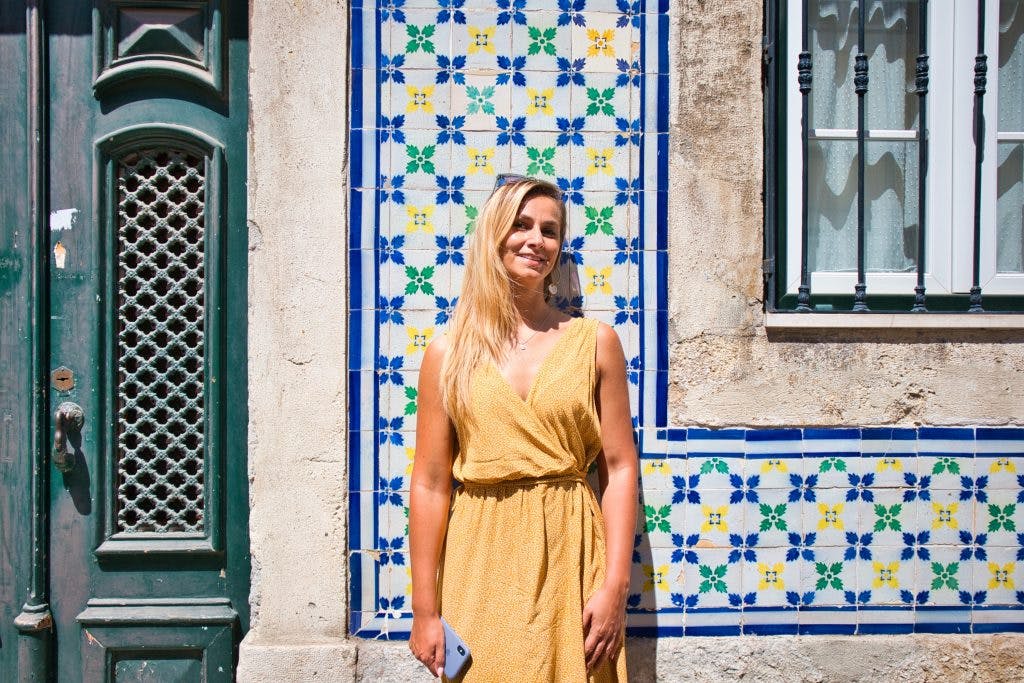 dziewczyna w żółtej sukience stoi na tle kolorowej ściany przed budynkiem w lizbonie