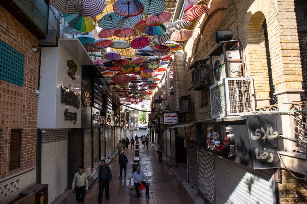 men and women walk along an alley in shiraz with umbrellas hanging over them