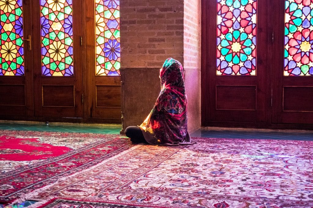 dziewczyna w hidżabie siedzi na podłodze w różowym meczecie w shiraz i patrzy zamyślona w stronę okna