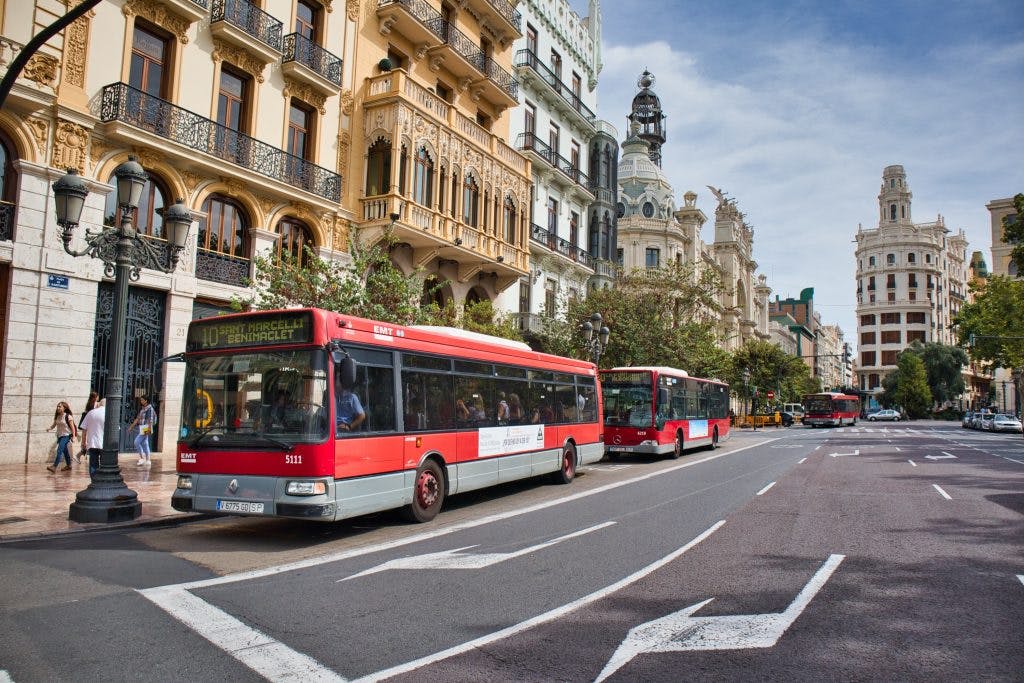 red bus on the street of valencia with white buildings in the back