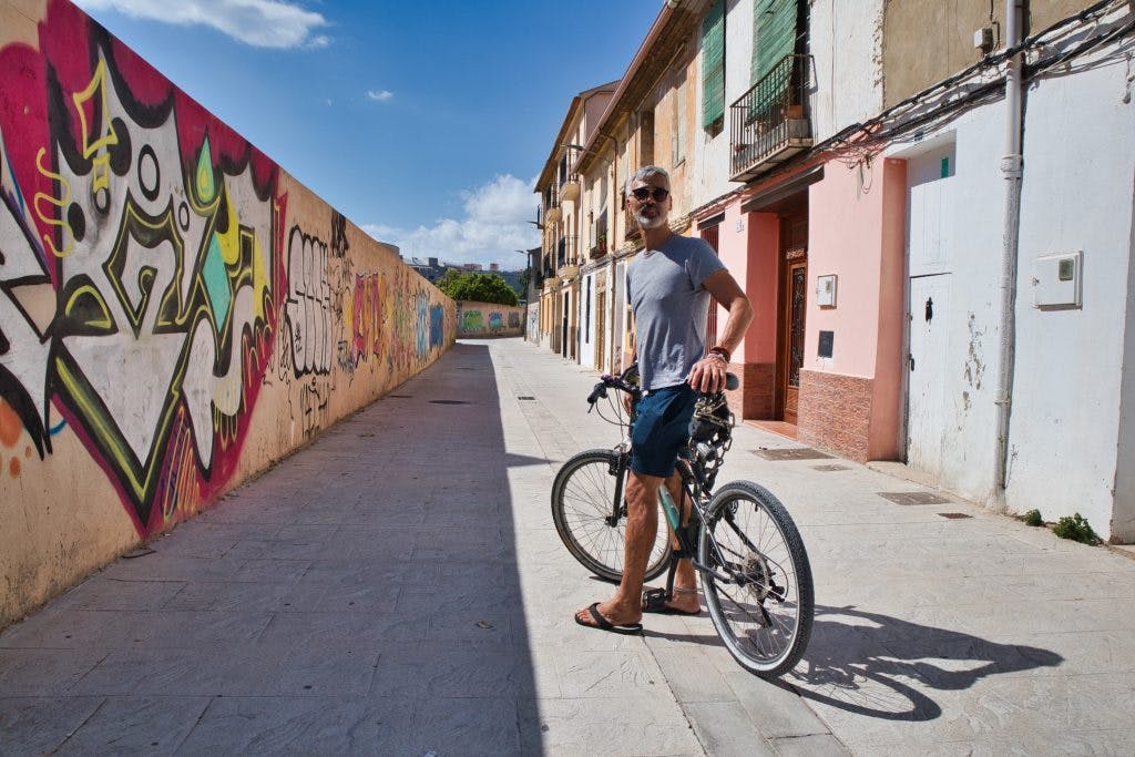 a man on a bike stands in a small side street in valencia spain