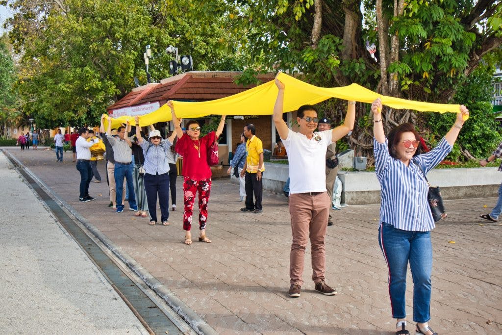 Thai people carrying a long yellow cloth above their heads at a temple in nakhon si thammarat