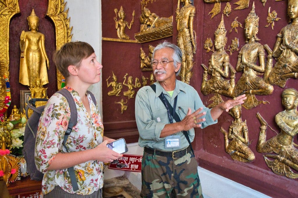 tajski mężczyzna pokazuje turystce z zachodu stiuk przedstawiający sceny z życia buddy 