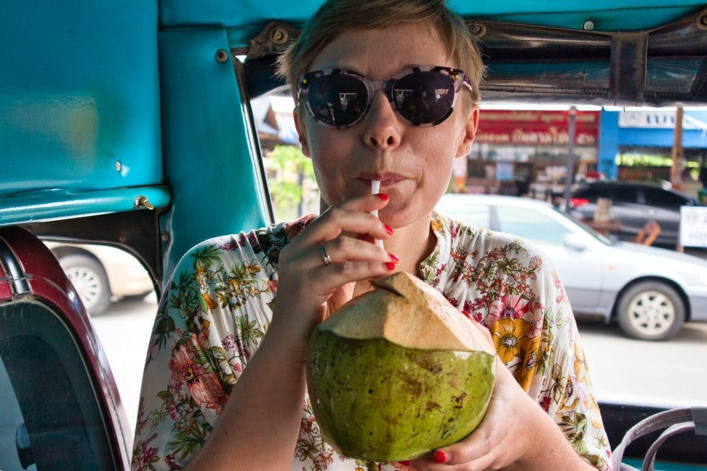 kobieta ubrana w kwiecistą bluzkę pije sok z kokosa w tajskiej taksówce 
